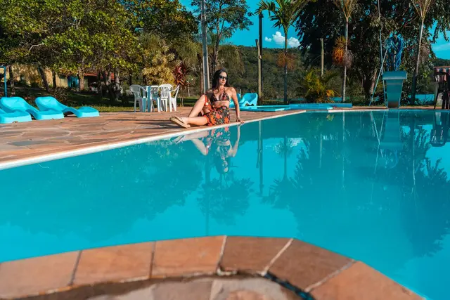 Piscina de água azul com espreguiçadeiras e reflexo da natureza na Pousada Solar Dona Dora
