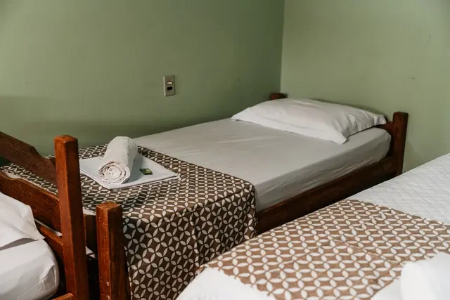 Quarto com duas camas de solteiro de madeira e enxoval branco na Pousada Solar Dona Dora