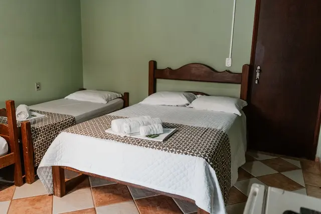Suíte com cama de casal e cama de solteiro, roupa de cama branca e piso de cerâmica