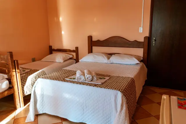 Suíte com cama de casal e camas de solteiro com enxoval e toalhas na Pousada Solar Dona Dora