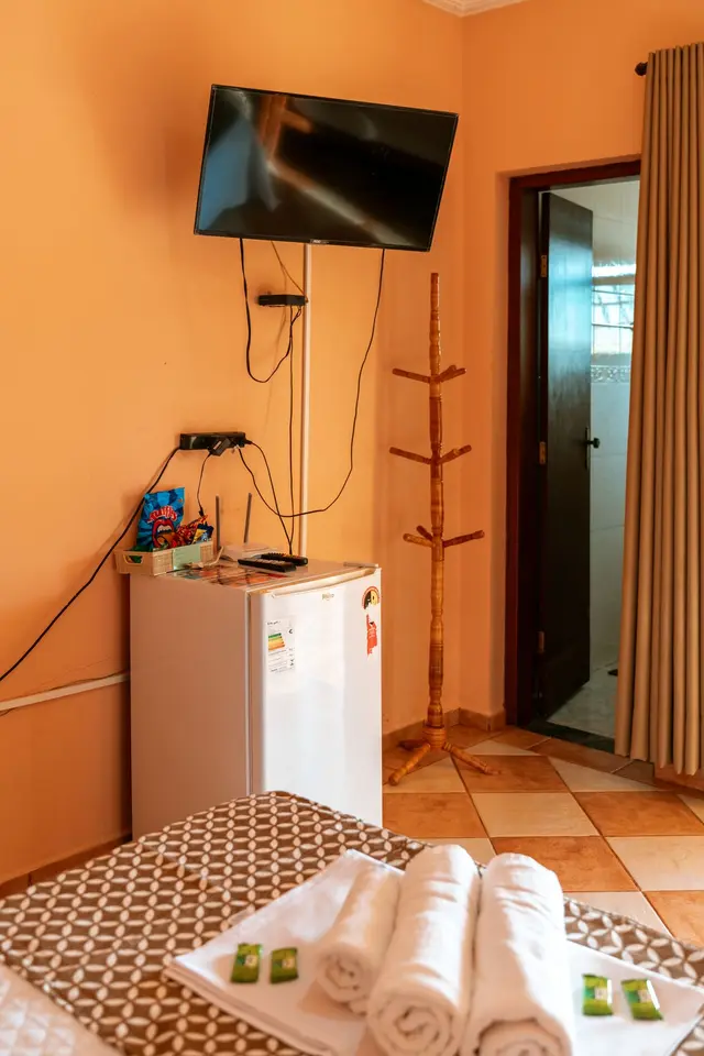 Detalhe da suíte com TV de tela plana, frigobar e acesso ao banheiro na Pousada Solar Dona Dora