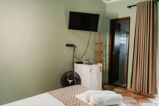 Suíte com TV na parede, frigobar, ventilador e banheiro privativo